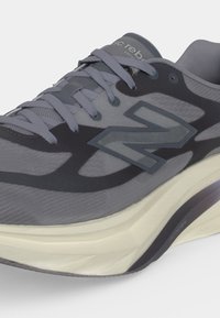 Γκρι και μαύρο αθλητικό παπούτσι New Balance με κορδόνια και παχιά λευκή σόλα, γωνιακά για να φαίνονται οι πλευρικές και μπροστινές λεπτομέρειες.