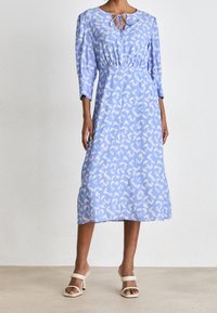 Modré šaty s vzorovaným designem v světlých odstínech. Mají kulatý výstřih s detaily na zavázání, tříčtvrteční rukávy a úzký pas.