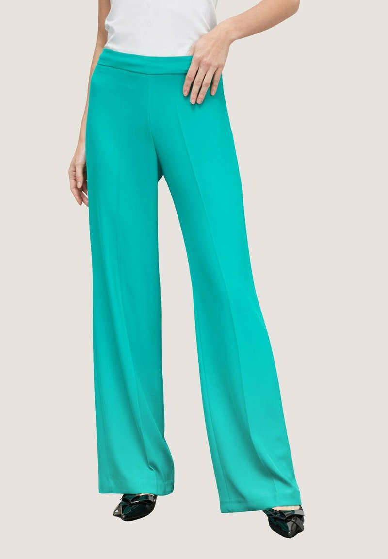 Aqua wijde broek van soepel materiaal, met een hoge tailleband en een vloeiende silhoeet. Gecombineerd met zwarte puntige schoenen.