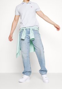 Světle šedý polo triko s malým logem, zkombinované se světle modrými džíny. Mátově zelená košile je uzlovaná v pase. Bílé tenisky.