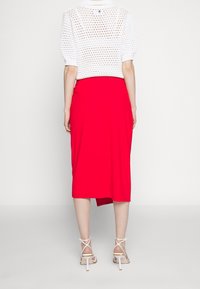 Witte gebreide top met korte mouwen en open weefsel, gecombineerd met een rode midi rok. De outfit wordt compleet gemaakt met witte gespenhakken.