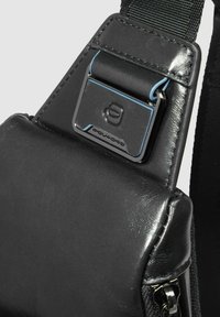 Borsa a tracolla in pelle nera con fibbia in metallo argentato con dettagli blu, superficie liscia e cuciture visibili sui bordi.