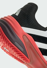 Schwarzer und weißer textiler Sportschuh mit roter Gummisohle. Verfügt über eine gerippte Textur, drei Streifen und "REPEATER+"-Branding auf der Sohle.