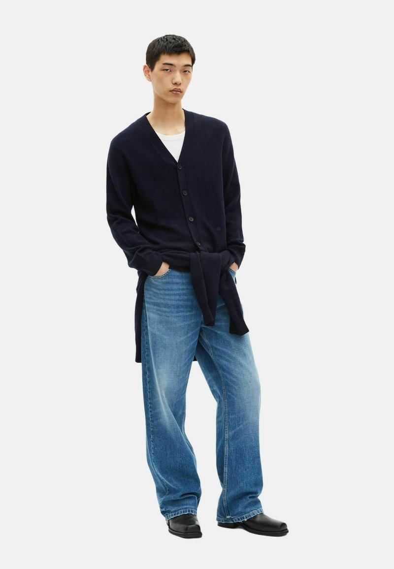 Navy cardigan with v-neck and button closure, paired with light blue wide-leg jeans and black shoes. Simple design, soft texture.