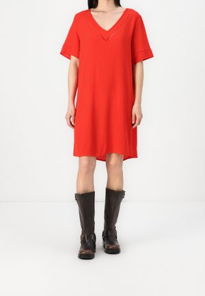Robe rouge à manches courtes avec un décolleté en V, en tissu léger et texturé, longueur mi-thigh, associée à des bottes brunes à genoux avec des boucles.