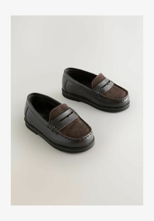 Ett par mörkbruna läder- och mockaloafers med sömnadsdetaljer och ett band över toppen, visade mot en ljus bakgrund.