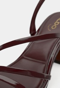 Sandale din piele lacuită burgundy cu design subțire cu bretele și textură netedă, lucioasă. Dispune de o talpă interioară căptușită și un toc subțiat.