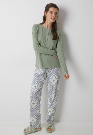 Lichtgroene blouse met lange mouwen en een henley-halslijn, gecombineerd met gestreepte pyjamabroekjes in wit, blauw en groen. Zachte, donzige groene slippers.