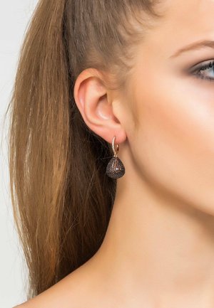 Orecchini a goccia che presentano una forma a goccia con una finitura scura e strutturata, accentuata da un anello dorato e piccole decorazioni trasparenti.