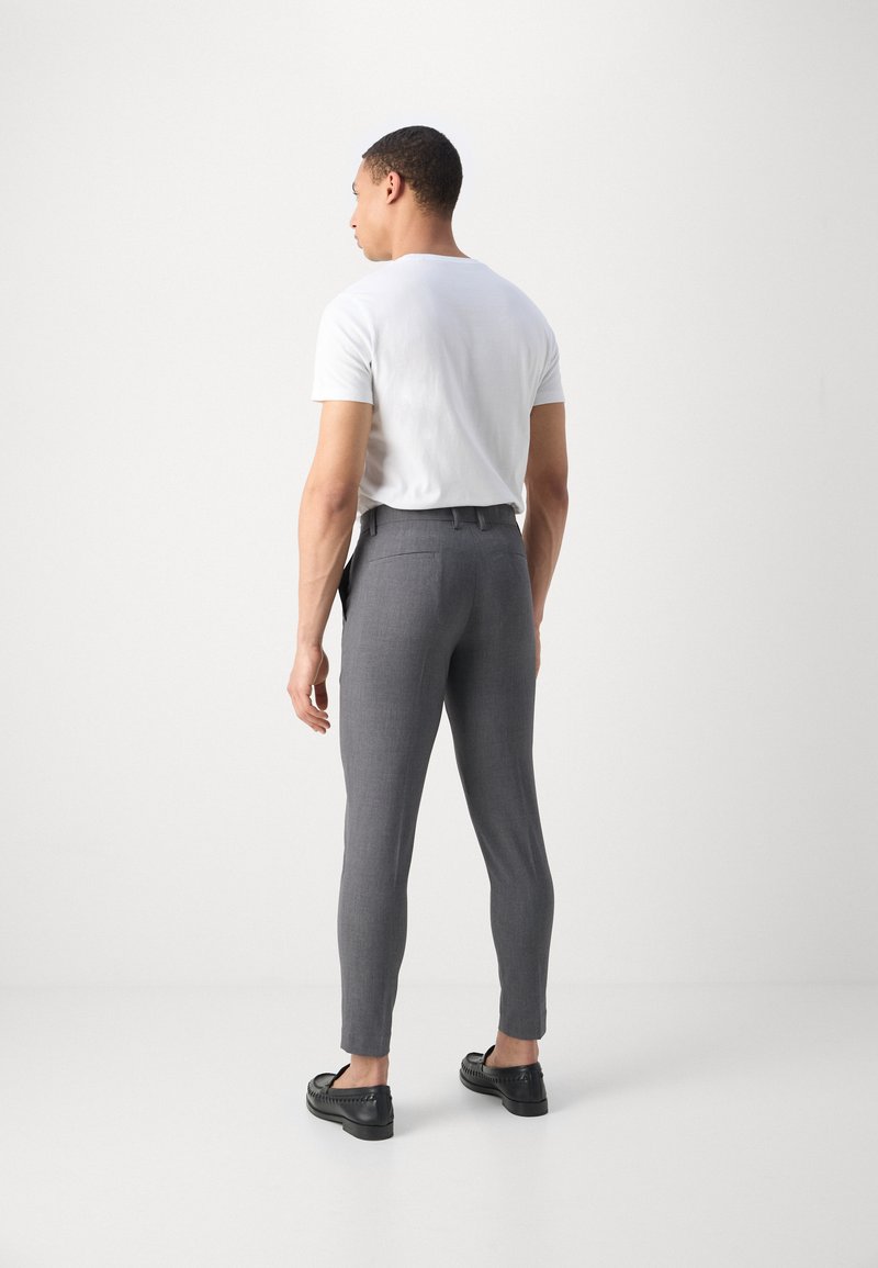 Pantaloni grigi su misura con una vestibilità aderente, caratterizzati da una texture liscia, passanti per la cintura e tasche posteriori, abbinati a una maglietta bianca semplice.