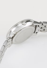 Montre en acier inoxydable argenté avec un boîtier rond, une lunette texturée et un bracelet en maillons métalliques, dotée d'une couronne sur le côté et d'un dos gravé.