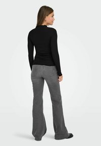 Top negro de manga larga con acabado texturizado, combinado con jeans acampanados grises. El conjunto presenta un diseño sencillo y una silueta ajustada.