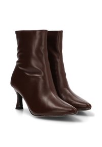 Par de botas de cuero marrón oscuro, hasta la mitad de la pantorrilla, con puntera afilada y tacones altos y finos, exhibidas sobre un fondo blanco.