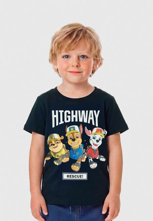 Šviesiaplaukis vaikas dėvi juodą marškinėlį, kuriame pavaizduoti trys animuoti gelbėjimo šunys geltonomis, mėlynomis ir raudonomis uniformomis su užrašu „HIGHWAY RESCUE!“