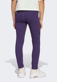 Lila leggings gjorda av elastisk tyg, med en slät yta och en figurnära design, kombinerade med vita sneakers med rosa detaljer.