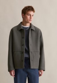 Grijze wollen jas met een kraag, knoopsluiting, twee voorzakken en een strakke, gestructureerde silhouette. G gedragen over een marineblauwe trui.