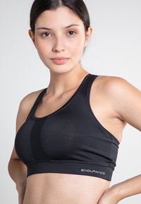 Svart sport-bh med racerback-design och texturerat tyg. Har en subtil logotyp på bandet och sömdetaljer. Lätt och kroppsnära passform.