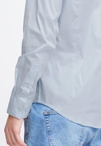 Lichtblauwe blouse met lange mouwen en een zachte textuur, met knopenmanchetten en een gebogen zoom, gecombineerd met vervaagde blauwe jeans.