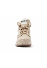 Zapatilla alta beige con suela de goma texturizada, cordones anchos y cuello acolchado. Presenta la etiqueta de la marca en la lengüeta y en el panel lateral.