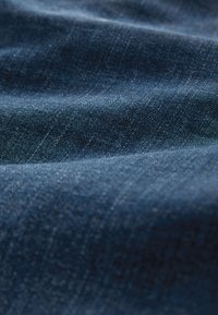 Prim-plan cu material denim albastru închis care arată textura detaliată a țesăturii și cute subtile.