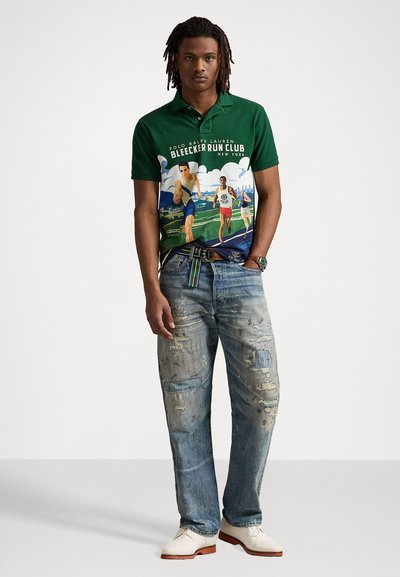 Polo verde con estampado gráfico de corredores; combinado con jeans azul desgastados y zapatos blancos, mostrando un estilo casual.