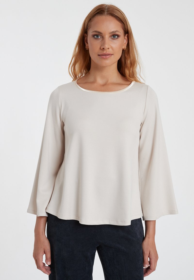 Lichtbeige langemouwen top met een ronde hals en uitlopende mouwen. Voordelige textuur, minimalistisch ontwerp en subtiele glans bij de halslijn.