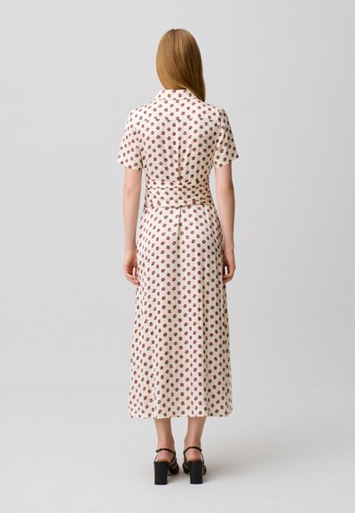 Donna con capelli lunghi e lisci che indossa un abito midi bianco a maniche corte con stampa floreale rossa e sandali neri con tacco largo, vista di spalle.