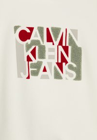 Felpa bianca con un design grafico testurizzato che presenta le parole "Calvin Klein Jeans" in lettere rosse, verdi e grigie.