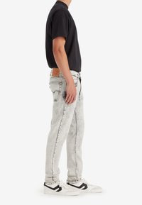 Svart kortärmad t-shirt, ljusgrå slitna jeans och vita sneakers med svarta detaljer. Anmärkningsvärd läderlapp på midjebandet av jeansen.