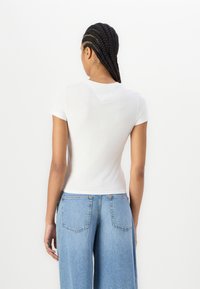 Camiseta blanca ajustada de manga corta, con una textura suave y un escote redondeado. Combinada con pantalones de mezclilla de talle alto en azul claro.