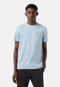 Světlomodré tričko s krátkým rukávem z měkké bavlny s malým logem na hrudi. Pohodlný střih s kulatým výstřihem a hladkou texturou.