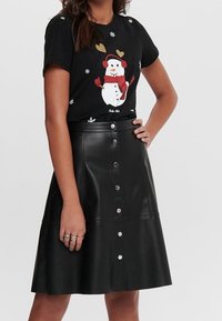 Sort t-shirt med et sne-mand grafik, der har hjerter og snefnug; parret med en knælængde sort faux lædernederdel med knapper.