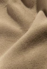 Beige stof med en blød, tekstureret overflade, der har en subtil glans og bløde folder, som udstråler et glat og varmt udseende.