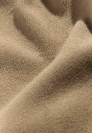 Tissu beige avec une surface douce et texturée, présentant un éclat subtil et des plis doux, affichant une apparence lisse et chaleureuse.