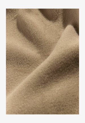 Tissu beige avec une surface douce et texturée, présentant un éclat subtil et des plis doux, affichant une apparence lisse et chaleureuse.