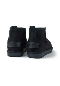 Botas de tobillo de ante negro con un tejido texturizado, paneles elásticos en los laterales y acentos de cuero negro con marca en el tacón. Suelas de goma plana.