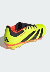 Crampon de football jaune avec des rayures et des accents noirs. Présente un dessus texturé, une semelle en caoutchouc et une doublure intérieure rouge vif.