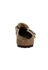 Sandale slip-on beige avec semelle en liège, tige en suède, sangle réglable et semelle texturée pour une meilleure adhérence et confort. Design à talon ouvert.