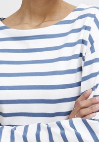 Blau-weiß gestreifter Langarm-Top mit Bootsausschnitt, aus weichem Stoff und lockerem Schnitt. Sichtbare Nahtdetails am Ausschnitt.