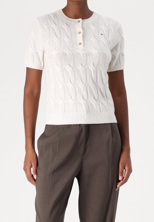 Witte kabelgebreide korte mouw trui met een ronde halslijn en een knoopsluiting met drie knopen, voorzien van geribbelde boorden en zoom.