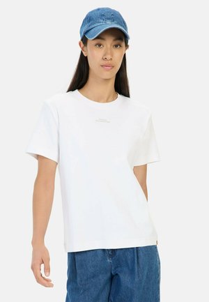Weißes Kurzarm-T-Shirt mit entspannter Passform, featuring einen schlichten Textdruck und kombiniert mit einer Denim-Kappe und hoch taillierten blauen Jeans.