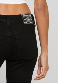 Melnas denim bikses ar augstu jostas vietu, redzamu šuvju un True Religion logo uzlīmi aizmugurē. Iekļauj standarta kabatas un pieguļošu dizainu.