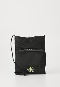 Svart nylon crossbody-veske med justerbar snorrem, frontlomme med glidelås, og fluorescerende logo-lapp på lærdetalj.
