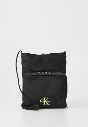 Black nylon crossbody bag with adjustable cord strap, front zip pocket, and fluorescent logo patch on leather accent.