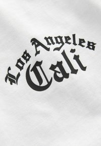 Bijela tkanina s mat teksturom koja prikazuje crni, podebljani tekst u gotičkom stilu koji glasi "Los Angeles Cali" s dekorativnim elementima.
