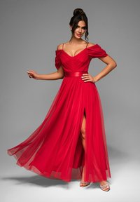 Robe de soirée rouge avec des manches dénudées, un corsage froncé, une jupe fluide et transparente, une fente sur le côté et une ceinture en satin. Chaussures : escarpins ornés.