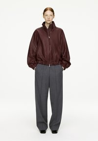 Burgundy leather bomber jacket with zip closure and elastic cuffs, paired with gray high-waisted wide-leg trousers. Smooth texture.