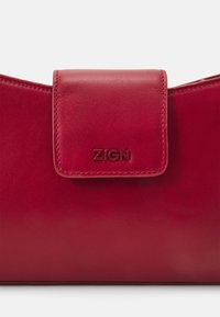 Červená kožená kabelka s hladkou texturou, vybavená přehýbací klopou a raženým logem "ZIGN". Jednoduchý, čistý design bez dalších ozdob.