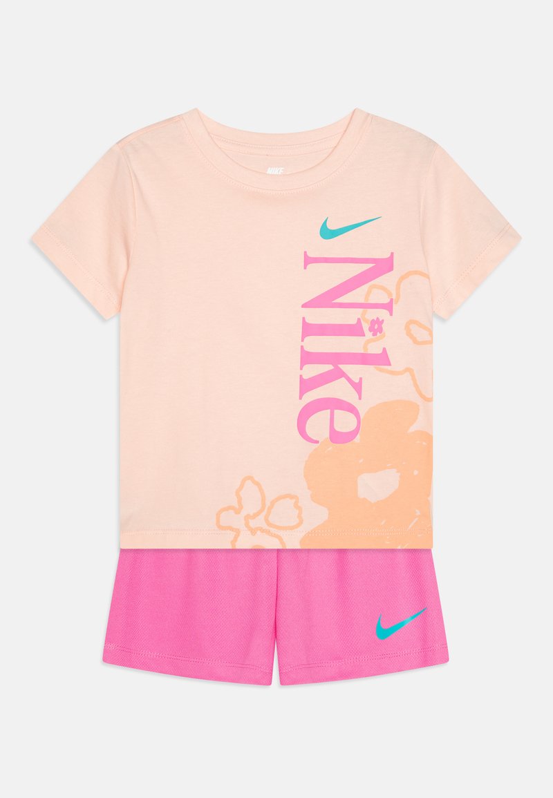 T-shirt de algodão rosa claro com um grande logótipo "Nike" colorido, combinado com calções de malha rosa brilhante que apresentam o swoosh turquesa da Nike de um lado.