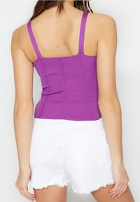 Débardeur violet à côtes avec des bretelles fines et une coupe ajustée, associé à un short en denim blanc effiloché avec des poches arrière.